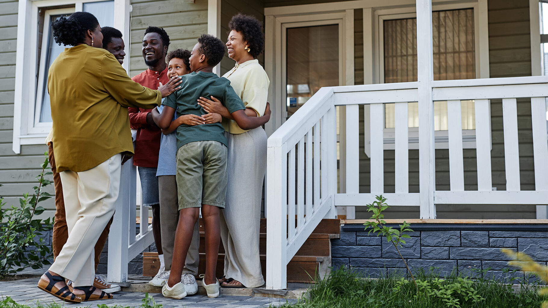 Black family gathering in front of a house, hugging each other and are happy.