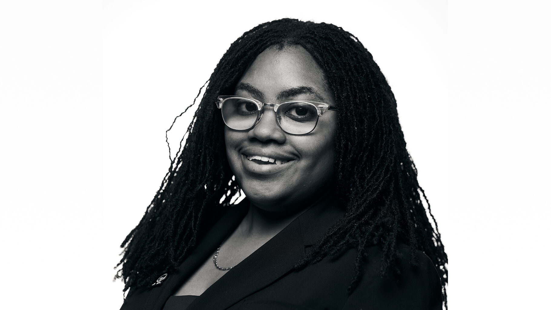 Black-and-white photo of Riana Medford, Class of 2027 at Howard University School of Law, and Summer Legal Intern at the Center for NYC Neighborhoods. Riana's hairstyle is braids and she's wearing eyeglasses. Riana is smiling in the photo.